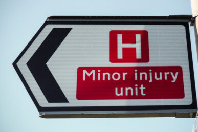 A road sign pointing to the left with the wording Minor injury unit in white text with a red background.
