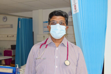 Photo taken of Consultant in plain clothes in a hospital ward with a stethoscope around their neck