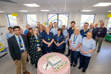 Group of uniformed and plainly dressed colleagues inside the new unit surrounding a celebratory cake on a table