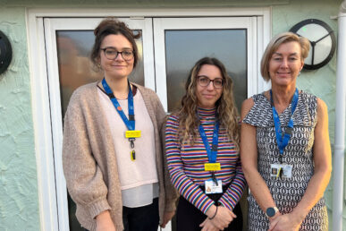 Three colleagues stood outside a green building. They are all smiling at the camera and all wearing the Somerset FT lanyards. the left colleague and the middle are wearing glasses.