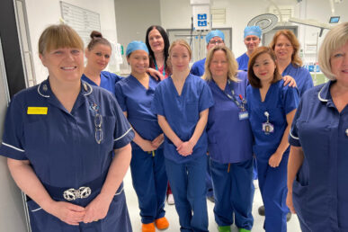 A group of colleagues in scrubs and medical uniforms in a clean and bright white hospital corridor