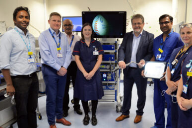 Peter lewis, chief executive of Somerset Foundation NHS Trust, with seven colleagues stood in front of a theatre style machine that has a scope attached showing microscopic images.