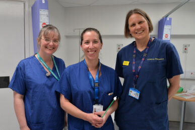 Doctor Jo Morrison, one of our consultant gynaecological oncologists, Doctor Holly Baker-Rand and Doctor Becky Newhouse, both specialty registrars and clinical fellows stood in a ward setting. They are all smiling to the camera in blue scrubs.