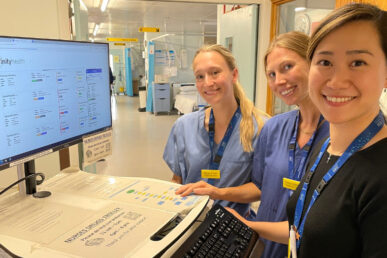 Three doctors stood next to a screen with an example of the Infinity Health system.