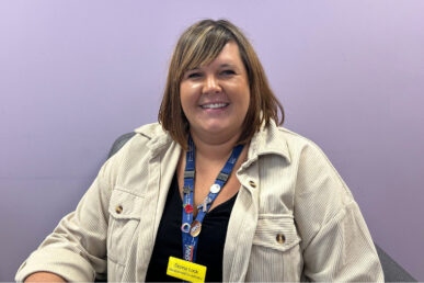 Colleague Donna Lock pictured sat against a purple backdrop