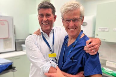 A photo of a surgeon and an anaesthetist standing in a hospital operating theatre.