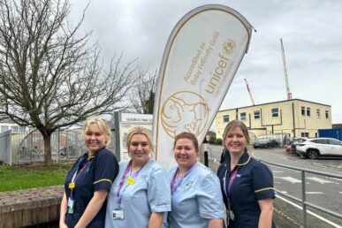 Five years of gold: celebrating continued excellence in baby care. Four maternity colleagues stood outside, in front of the gold UNICEF flag. They are all smiling.